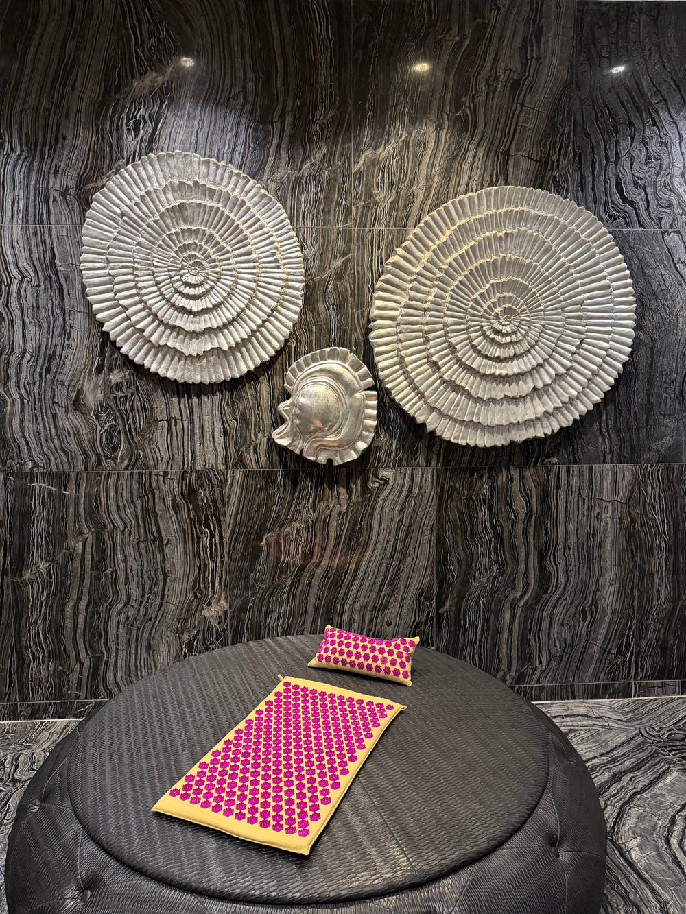 The LotuSun mat and pillow resting on a round black ottoman against dark carved stone