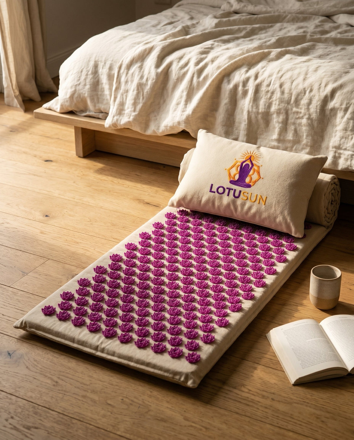 LotuSun mat unrolled on an oak floor beside a low platform bed in late afternoon light, with a ceramic vessel and open book nearby.
